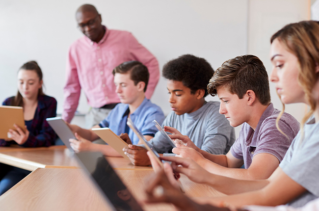 An educator watches over middle school students working on their devices