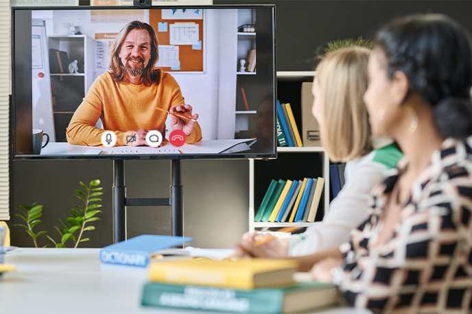 A group of students watching a monitor with a virtual instructor presenting on it